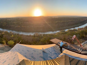 Hunter Roofing crew installing a metal roof at sunset above a river valley